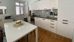 Moderni keittiö, jossa on valkoiset kaapit, graniittitaso ja ruokapöytä, jonka päällä on kulho täynnä hedelmiä.