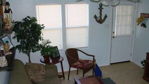 A living room with a sofa, armchair, coffee table, potted plants, and a door with a sign.