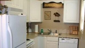 A compact kitchen with white cabinetry, a refrigerator, a dishwasher, and a sink.