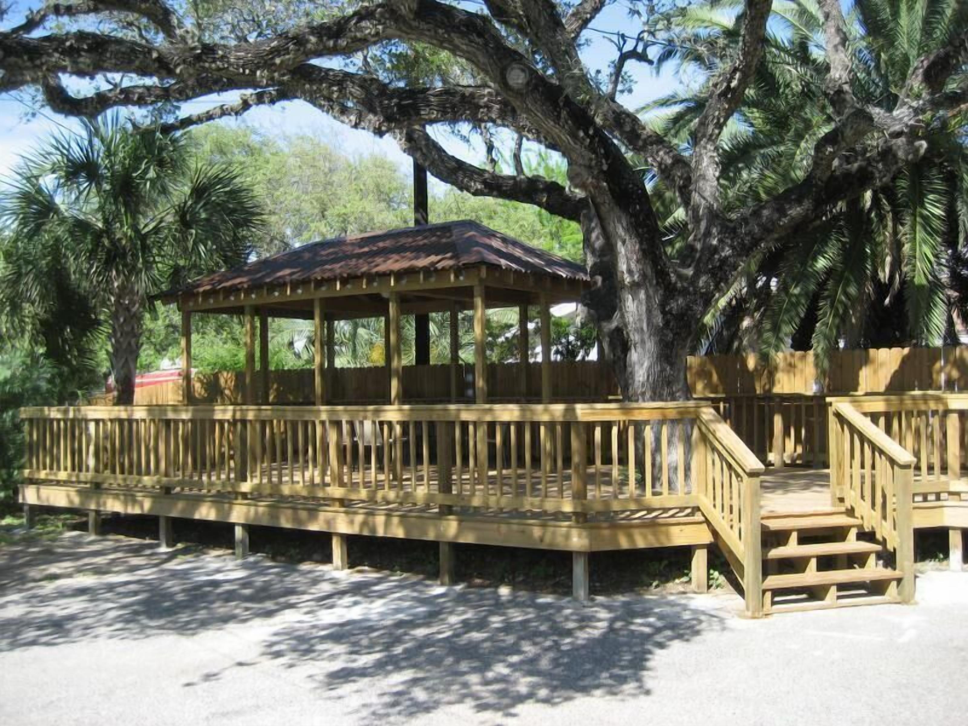 A wooden gazebo with a roof, surrounded by trees and a wooden deck.