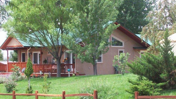 Una casa de dos pisos con un porche, un patio cercado y un pequeño árbol en primer plano.