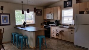 Una cocina con una isla central, taburetes azules, armarios de madera, un microondas, una estufa y un refrigerador.