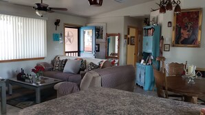 Un salón acogedor con un sofá, una mesa de centro y una mesa de comedor con sillas. Se observa un aparador azul con adornos y un cuadro en la pared.