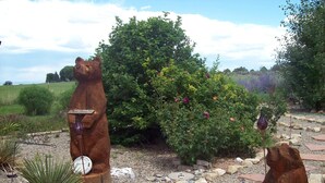 Un jardín con dos esculturas de madera de osos, un letrero de bienvenida y una variedad de plantas y flores.