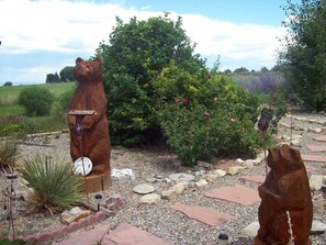 Un giardino con due sculture di orsi in legno, un cartello di benvenuto e diverse piante e fiori.
