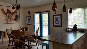 Una cucina con un piano di lavoro in granito, sedie di legno, un tavolo da pranzo, lampade a sospensione e un'ampia finestra con persiane.
