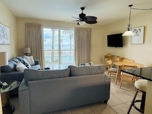 Een woonkamer met een bank, een televisie, een eettafel met stoelen en een balkon met gordijnen.
