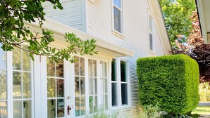 A house with a white exterior, large windows, and a well-maintained garden with various plants and a neatly trimmed hedge. - Beautiful Chico Farmhouse With Room for All…10 beds!! (Chico)