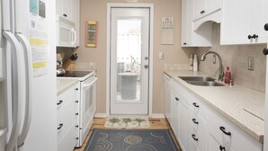 A compact kitchen with white cabinets, a microwave, a sink, and a door with a view of the outside. - SeaPines, Short walk to the beach, Pet friendly, 2 free bicycles (hilton head)