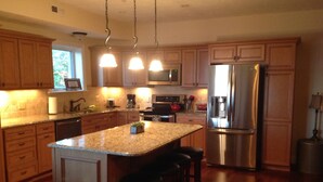 A modern kitchen with wooden cabinets, stainless steel appliances, and a central island with stools. - LAKEFRONT CONDO#111 3BR/2BA-private beach, indoor pool  Rent 3 get 4th free-ask (Geneva on the Lake)