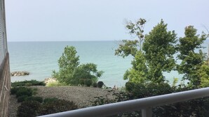 A balcony with a view of the sea and surrounding greenery. - LAKEFRONT CONDO#111 3BR/2BA-private beach, indoor pool  Rent 3 get 4th free-ask (Geneva on the Lake)