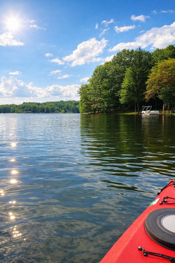 Ein ruhiger See mit einem roten Kajak im Vordergrund und einer bewaldeten Uferlinie im Hintergrund.
