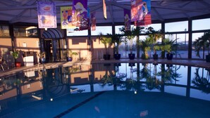 An indoor swimming pool with clear reflections, surrounded by potted plants and a large window. - Oceanfront Penthouse, great views, Best Amenities, Spacious Sleeps 14, 3 Pools (Ocean City)