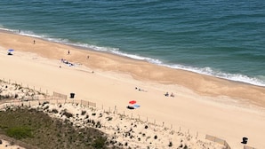 A beach with a sandy shore, a few umbrellas, and a fence along the edge. - Oceanfront Penthouse, great views, Best Amenities, Spacious Sleeps 14, 3 Pools (Ocean City)