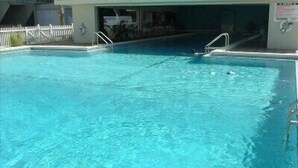 Une piscine avec une eau d’un bleu limpide, une clôture blanche et un bâtiment en arrière-plan.