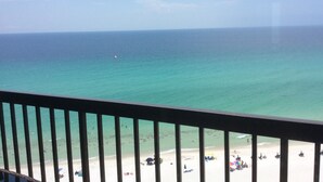 Une vue sur la plage depuis un balcon doté d’une balustrade, avec un ciel dégagé et une mer calme.