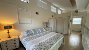A bedroom with a bed, nightstands, a lamp, a wardrobe, and a window with blinds. - Beautiful Beach House with large pool (Boca Grande)