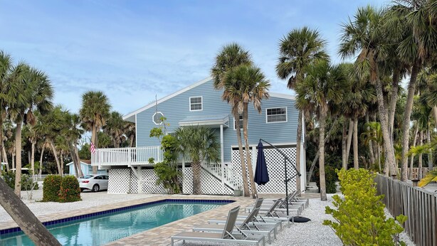 A pool area with lounge chairs, a pool, and a house with a white fence. - Beautiful Beach House with large pool (Boca Grande)