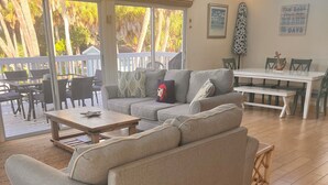 A living room with a grey sectional sofa, a wooden coffee table, and a dining table with chairs. There is a sign above the window that reads "BEACH HOUSE". - Beautiful Beach House with large pool (Boca Grande)