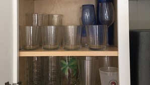 A cabinet with shelves holding various glassware, including tumblers, wine glasses, and decorative bottles. - Beautiful Beach House with large pool (Boca Grande)