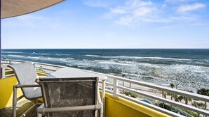 A balcony with a view of the ocean, a chair, and a table.