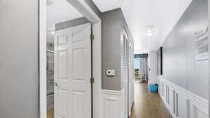 A hallway with a white door, a thermostat, and a blue trash bin.