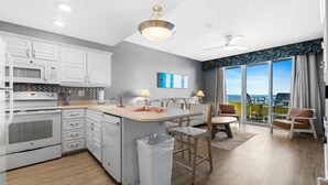 A modern kitchen with white cabinets, a built-in oven, and a large island with a trash bin.