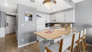 Una cocina moderna con armarios blancos, una isla central con taburetes altos y una lámpara colgante.