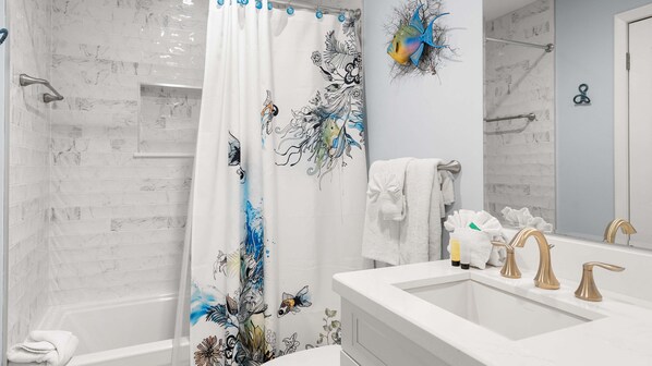 A bathroom with a shower curtain featuring aquatic designs, a bathtub, a sink with gold faucets, and a towel rack.