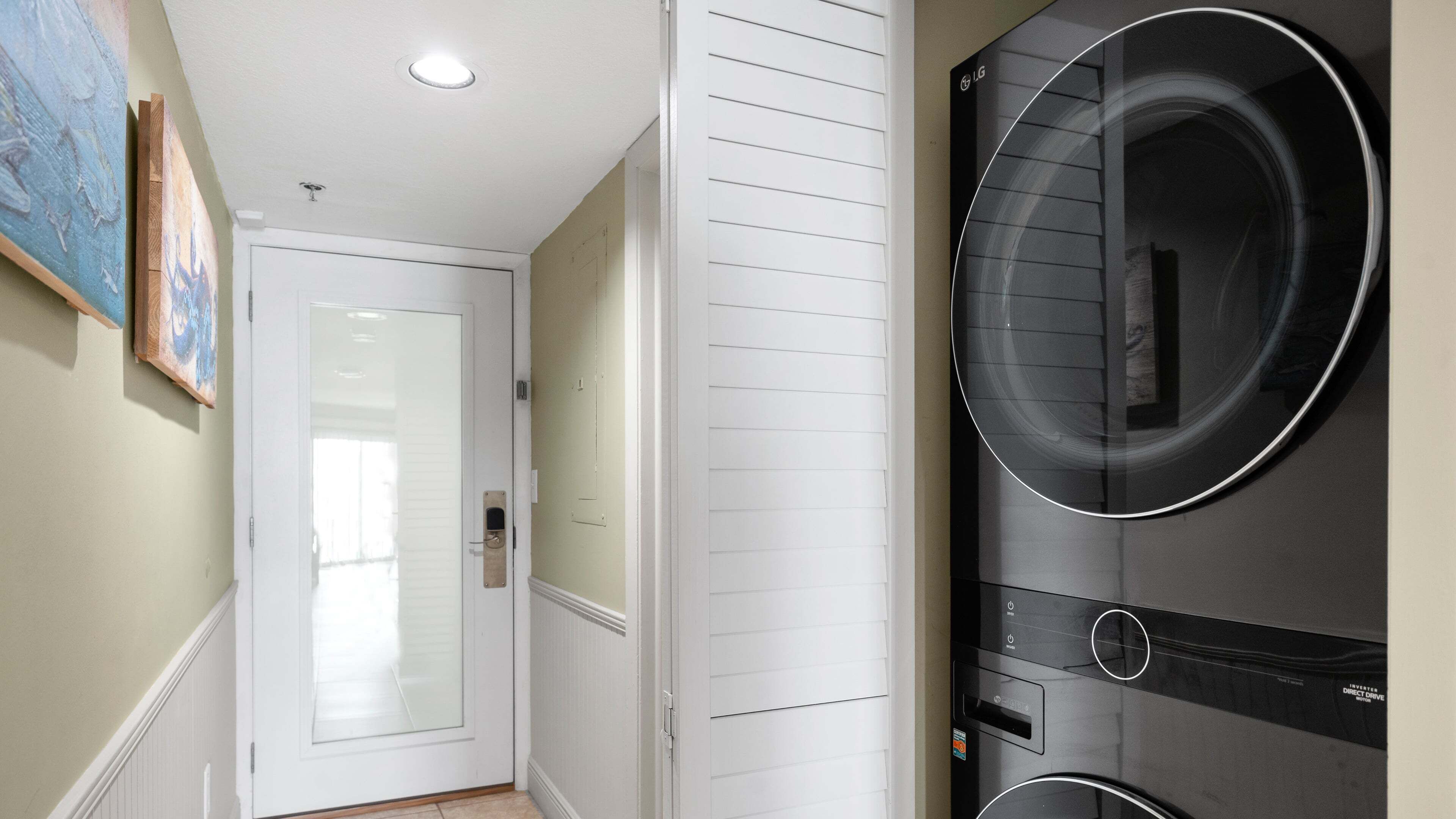A laundry room with a large black washer and dryer, a white door, and a painting on the wall.