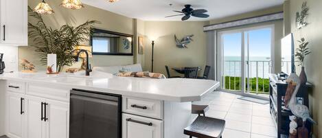 A modern kitchen with a large island, pendant lights, and a view to the outside.