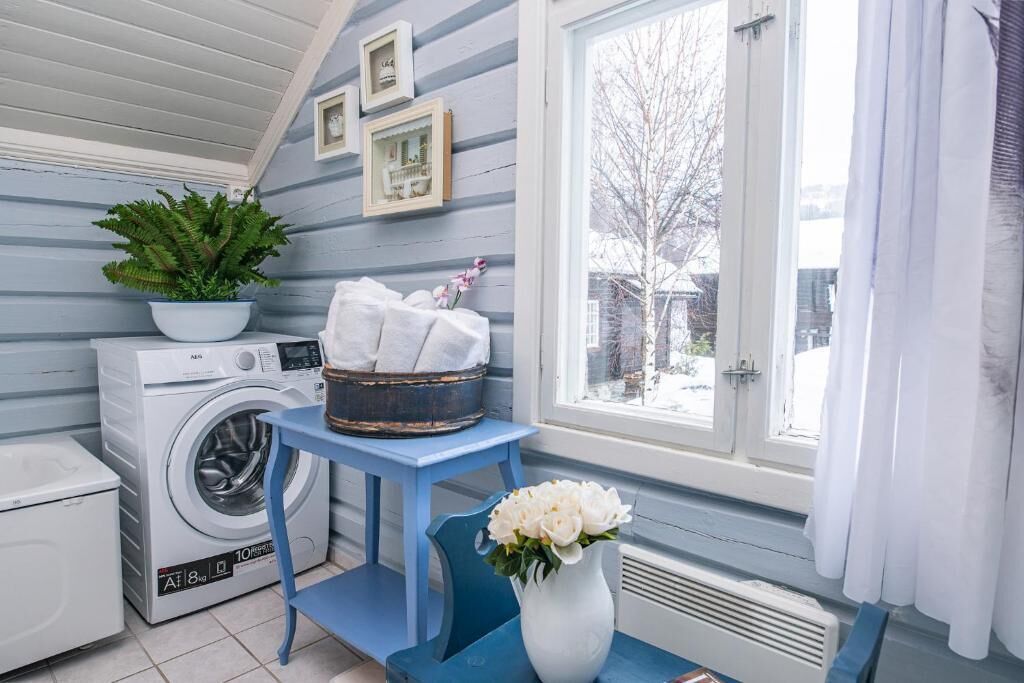 A laundry room with a washing machine, a drying rack, a potted plant, and a vase with flowers.