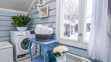 A laundry room with a washing machine, a drying rack, a potted plant, and a vase with flowers.