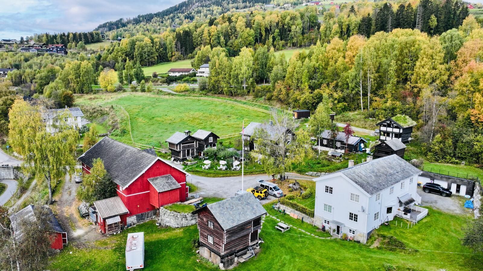 Un pueblo rural con casas de madera tradicionales, un granero rojo y un edificio blanco con un amplio porche.