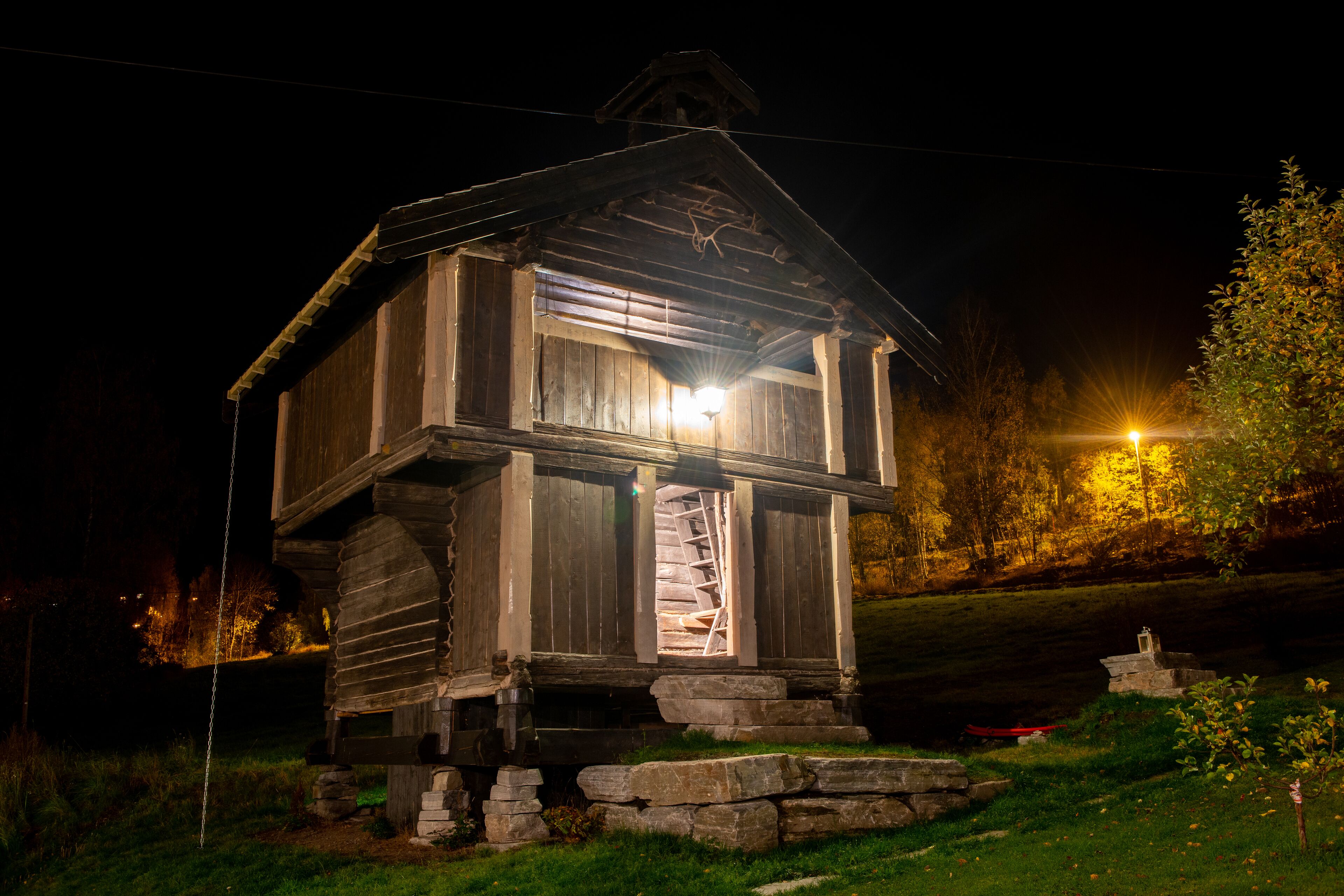 A rustic wooden cabin with a spiral staircase, surrounded by a stone foundation and a grassy area.
