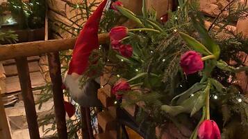 Et rustikt interiør med en stenvæg, en trætrappe og et juletræ pyntet med lys og røde tulipaner.