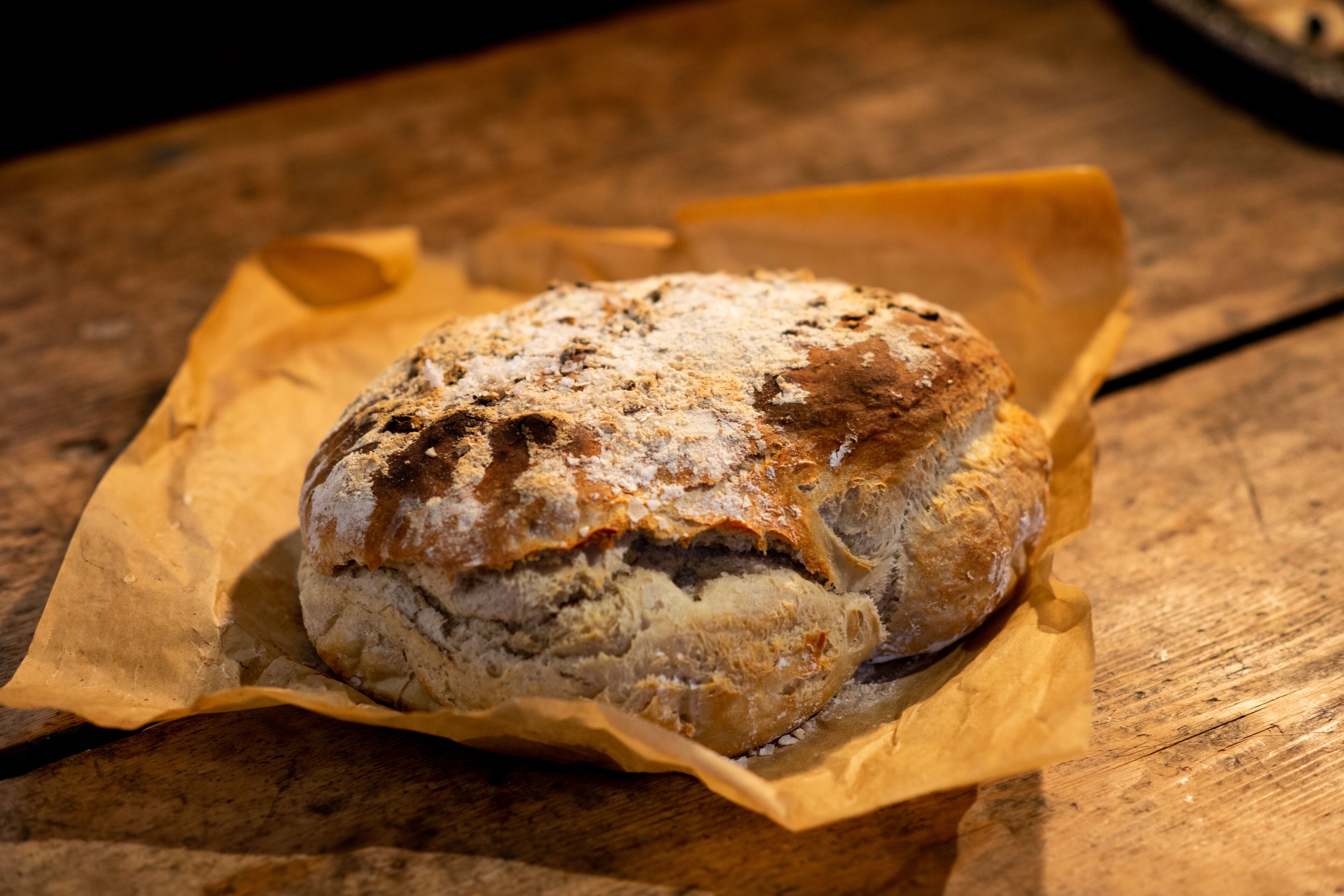 A loaf of bread on a wooden surface with a piece of parchment paper underneath.