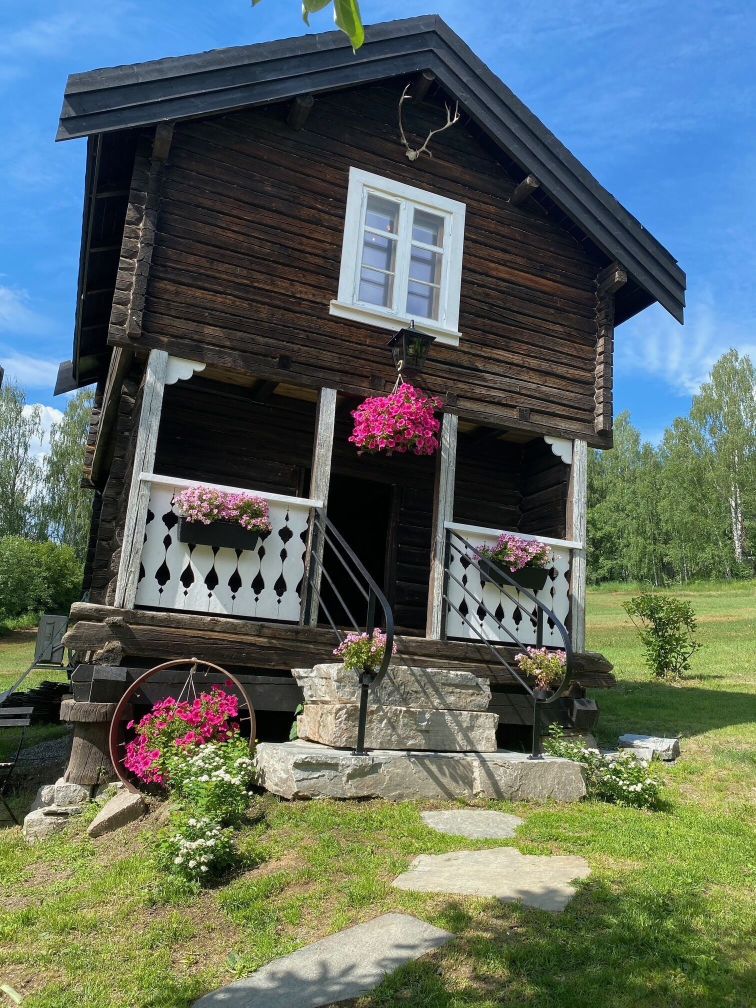 Une maison de campagne en bois, dotée d’un porche, d’un escalier en pierre et de jardinières suspendues.
