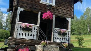 Une maison de campagne en bois, dotée d’un porche, d’un escalier en pierre et de jardinières suspendues.