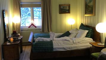 A bedroom with a bed, two bedside lamps, a window with curtains, a painting on the wall, and a patterned rug.