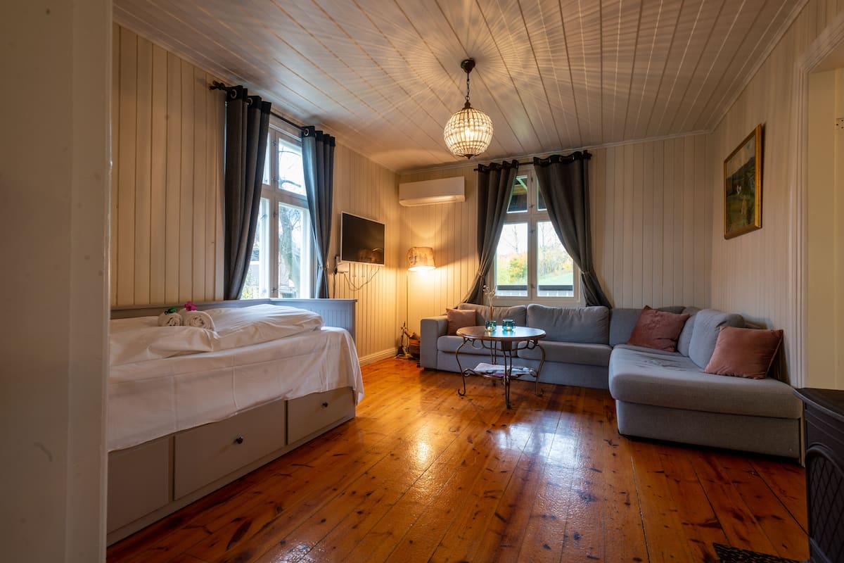 A room with a bed, a sofa, a small table, and a lamp.