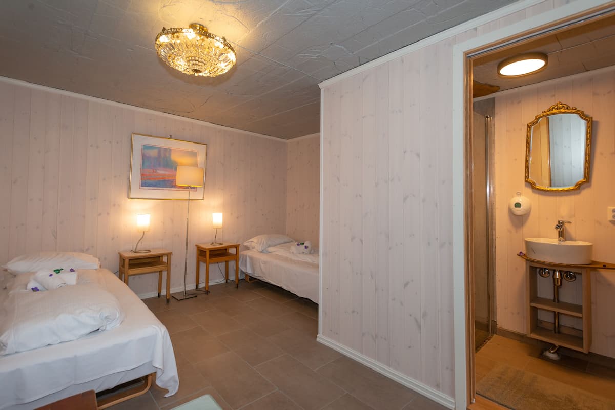 A hotel room with two beds, a bedside table with a lamp, a framed picture on the wall, and a bathroom with a mirror and sink.