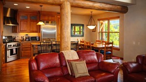 A spacious living room with a red leather sofa, a wooden dining table with chairs, and a kitchen area with wooden cabinets and stainless steel appliances.