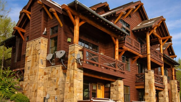 A large log cabin with a stone foundation, multiple balconies, and satellite dishes.