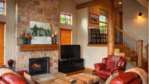 A stone fireplace, a television, leather sofas, and a staircase.