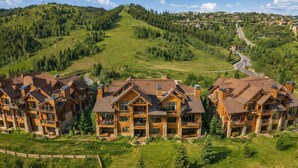 A large log cabin-style hotel with multiple guest rooms, situated on a hillside with a view of a winding road and surrounding greenery.