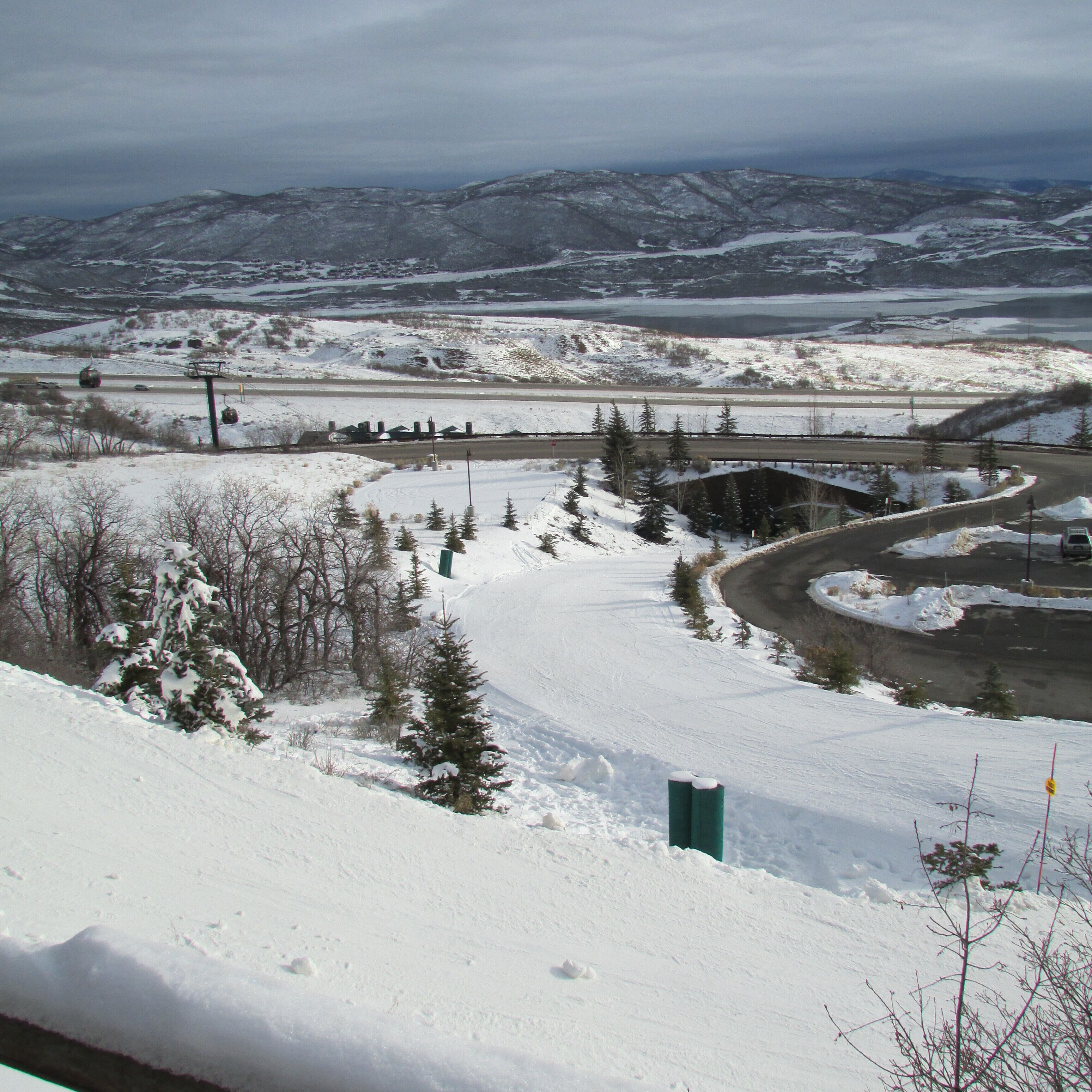 A snowy landscape with a road curving through it, surrounded by trees and mountains in the distance.