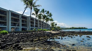 Un hôtel à étages, situé sur une côte rocheuse et bordé de palmiers.