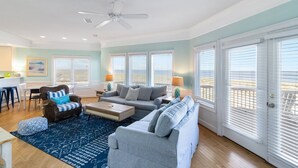 A spacious living room with a grey sofa, a blue patterned rug, and a dining area with a white table and chairs. - Oceanview with Sunrise Views, Direct Beach Access & Hot Tub (Tybee Island)