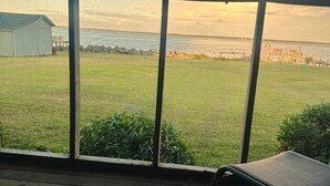 Vista desde una habitación con amplios ventanales que dan a un césped con un cuerpo de agua y un muelle.